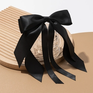 Detail of elegant black satin bow hair clip with long ribbons on a wooden tray