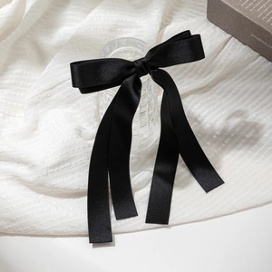 Detail of elegant black satin bow hair clip with long ribbons on a glass surface