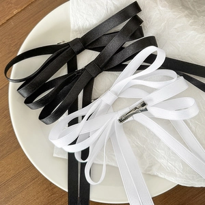 Elegant black and white satin bow hair clips with long ribbons on a ceramic plate