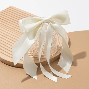 Close-up of elegant cream satin bow hair clip with long ribbons on a glass vessel