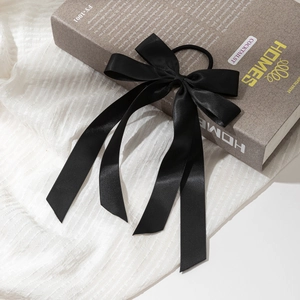 Détail d'un chouchou élégant en satin noir avec longs rubans sur un livre décoratif