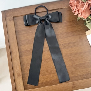 Détail d'un chouchou élégant en satin noir avec longs rubans sur plateau en bois