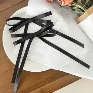 Detail showing a pair of elegant black satin bow hair clips with long flowing ribbons