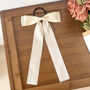 Détail d'un chouchou à nœud crème avec de longs rubans sur une surface en bois