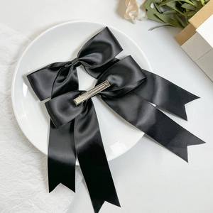 Elegant black satin bow hair clips with long streamers on white porcelain tray