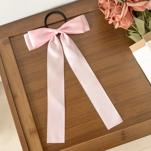 Chouchou élégant en satin rose avec long ruban posé sur un plateau décoratif en bois
