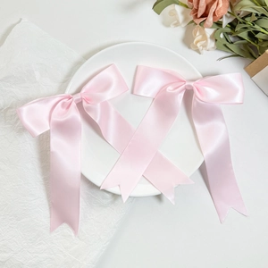 Pair of light pink satin bow hair clips with elegant long tails on a white plate