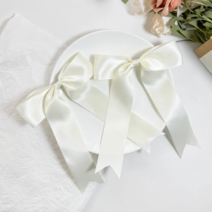 Detail view of two cream satin bow hair clips with long tails on a white decorative plate