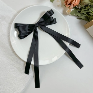 Close-up of elegant double-layered black satin bow hair clip with long ribbons on white plate
