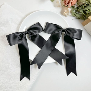 Close-up of a pair of black satin bow hair clips with long streamers on a white plate