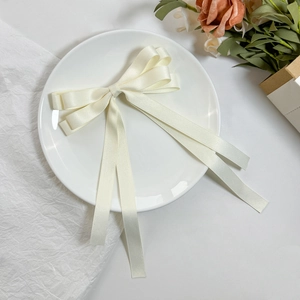 Elegant cream satin double-layered bow hair clip with flowing ribbons on white plate