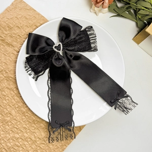 Detail of black satin bow hair clip with lace edges and sparkling heart rhinestone