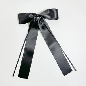 Close-up of a large black satin bow hair clip with elegant long ribbons on white background