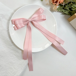 Elegant pink satin double-layered bow hair clip with long ribbons on a ceramic plate