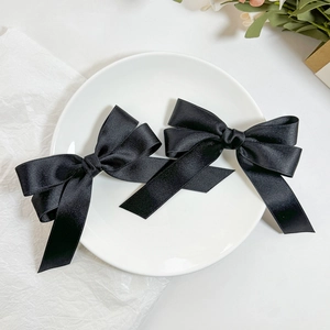 Elegant pair of black satin bow hair clips with long ribbons on white ceramic plate