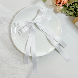 Macro detail of white satin double-layered bow hair clip with elegant long flowing ribbons