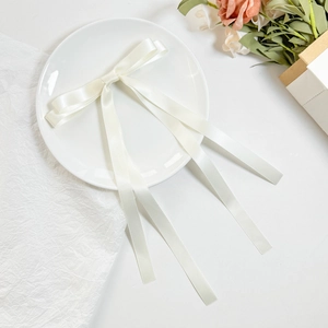 Elegante fermaglio per capelli con doppio fiocco in raso crema e lunghi nastri su un piatto