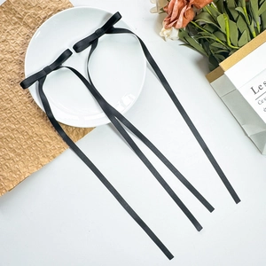 Macro shot of two black satin ribbon bow hair clips with long streamers on a white plate