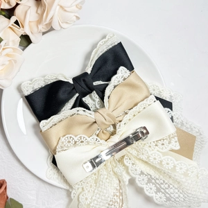 Elegant lace satin bow hair clips in black, champagne and cream displayed on a ceramic tray
