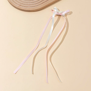 Close-up of pink and white ribbon bow hair clip with long streamers on wooden tray