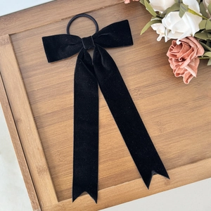 Elegant black velvet bow hair tie with long streamers on a rustic wooden tray