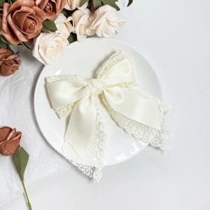 Elegant cream lace bow hair clip with satin ribbon and embroidery in a decorative tray