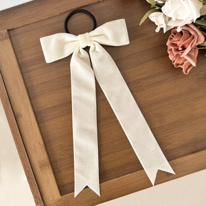 Close-up of cream velvet bow hair tie with long ribbons on a wooden tray