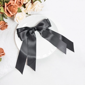 Detail of elegant black double-layered satin bow hair clip with long silk ribbons