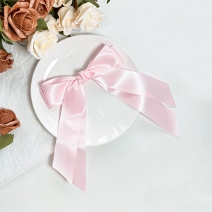 Elegant large pink satin bow hair clip with long ribbons on a decorative white ceramic plate