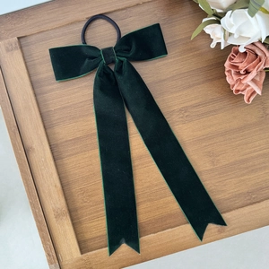 Detail view of dark green velvet bow hair tie with long ribbons on a wooden tray