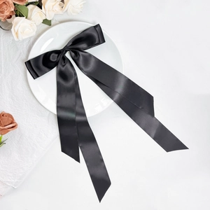 Detailed view of an elegant black satin bow hair clip with long ribbons on a white plate