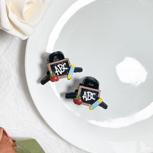 Dettaglio di mini mollette per capelli a tema scuola con lavagna ABC e icone mela