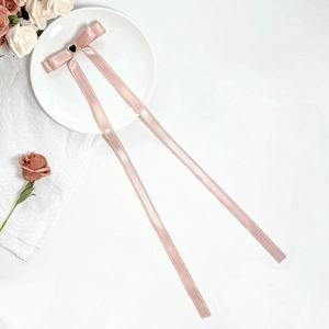 Pink ribbon bow hair clip with heart rhinestone accent on a minimalist white ceramic plate