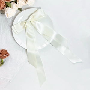 Close-up of elegant cream satin bow hair clip with long ribbons on a white decorative plate