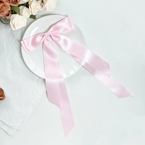Elegant pale pink satin bow hair clip with long ribbons on white decorative plate