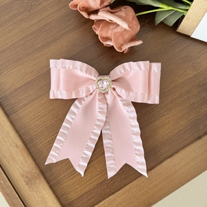 Pink satin bow hair clip with heart rhinestone on a vintage dark wood surface