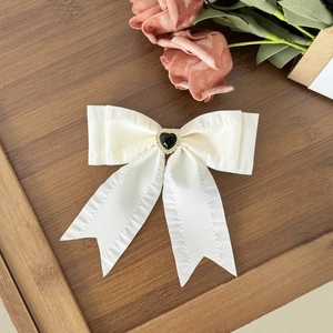 Detail of cream white bow hair clip with black heart rhinestone and gold trim finish