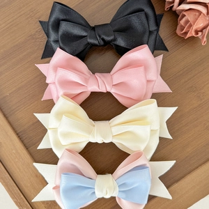 Elegant satin bow hair clips in black, pink, and beige displayed on a wooden tray