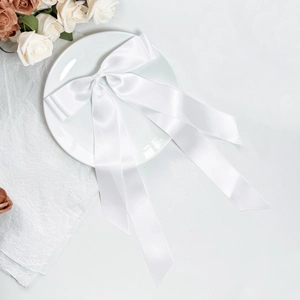 Detailed view of white satin bow hair clip with long ribbons on an elegant ceramic plate