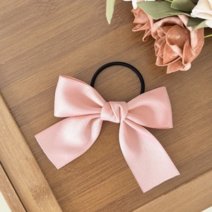 Pink satin bow hair tie with elastic band on a rustic wood background with floral decor