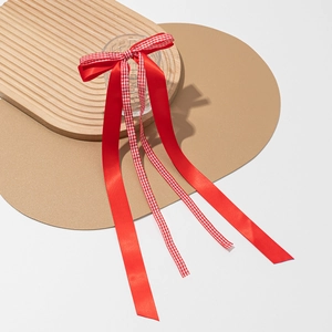 Détail de la barrette à nœud en satin rouge et ruban à carreaux sur plateau en bois