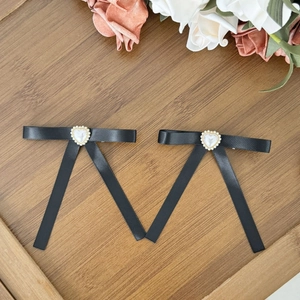Détail de barrettes nœuds en ruban noir avec perles en cœur sur un plateau en bois