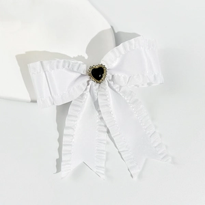 Detailed close-up of white ruffled ribbon bow hair clip with rhinestone heart centerpiece