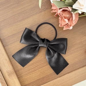 Detail of elegant black satin bow hair tie on a wooden tray with decorative roses