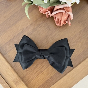 Detailed close-up of double-layered black satin bow hair clip on a wooden tray