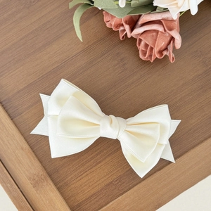 Detail of elegant cream satin bow hair clip on a wooden tray with decorative roses