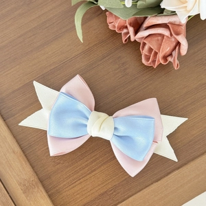 Close-up of a layered pink and blue satin bow hair clip on a vintage wooden tray