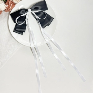 Elegant black and white bow hair clip with long ribbons on a ceramic plate