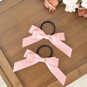 Chouchous à nœuds en satin rose avec élastiques noirs présentés sur un plateau en bois
