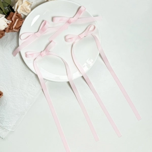 Close-up of four pink grosgrain ribbon bow hair clips with long streamers on white decor